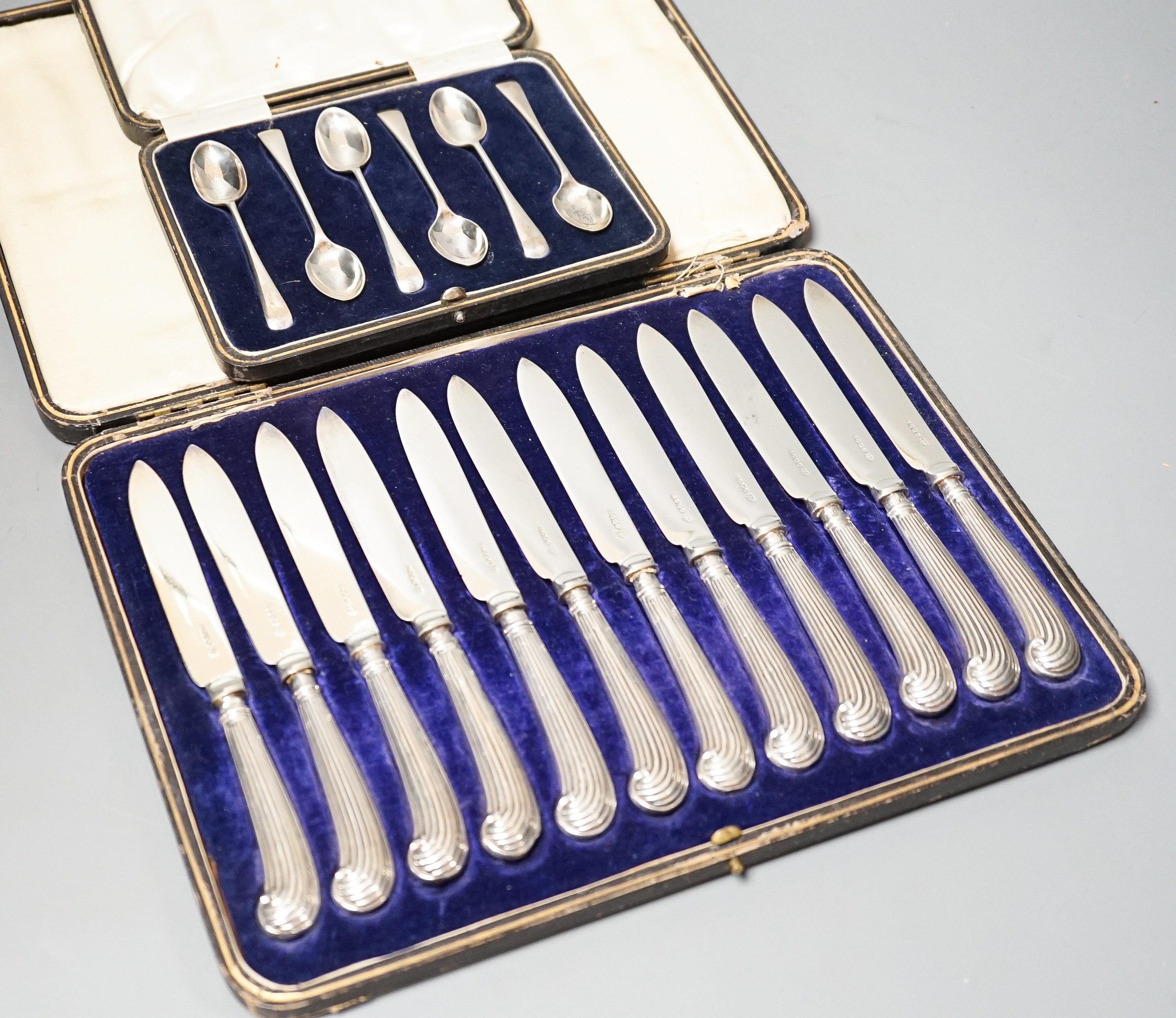 A cased set of twelve reeded silver pistol handled steel dessert knives and a cased set of six silver teaspoons.